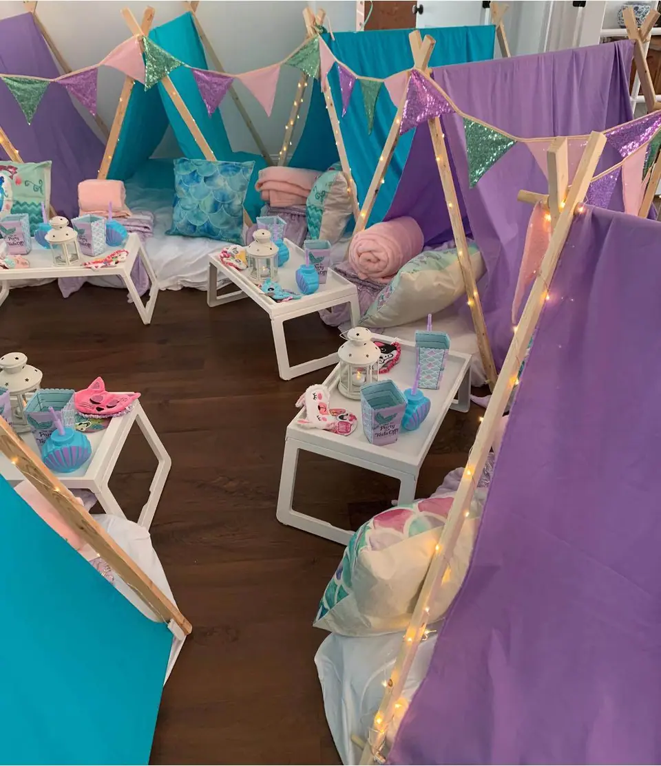 Indoor children's party setup with small teepees decorated with fairy lights, and tables set with teacups and saucers.