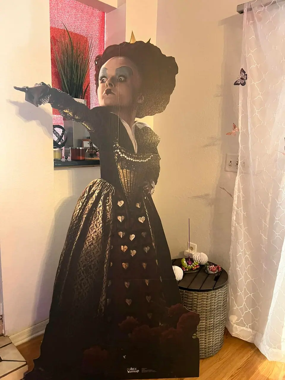 Cardboard cutout of a woman dressed in an elaborate Victorian gown and hat, pointing outward, standing in a Wonderland Wonders party interior.