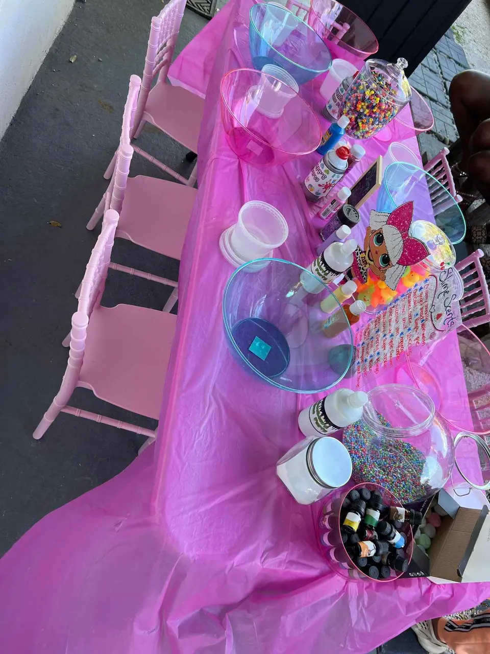A table covered with a pink cloth, displaying various bottles of sprinkles and toppings for ice cream or desserts, perfect as a Birthday Party upgrade.