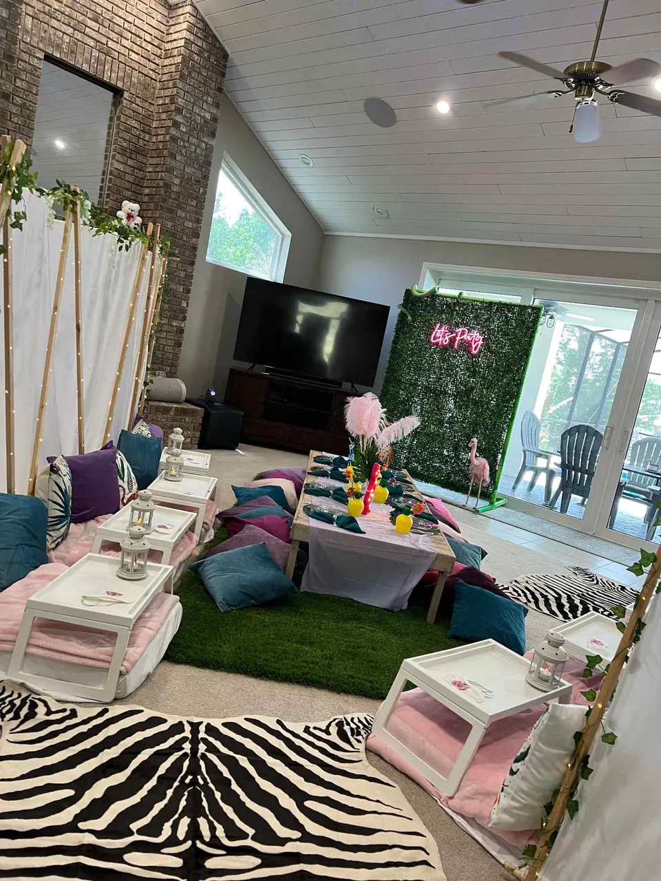 Living room decorated for a tropical slumber party with low seating, zebra print rugs, and a pink floral backdrop.
