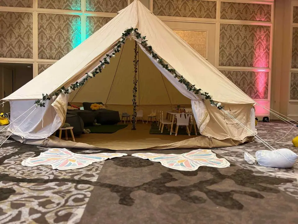 A large indoor glamping tent decorated with string lights and garlands, set up with a cozy seating area inside, on a patterned carpet, perfect for any Central Florida corporate event.