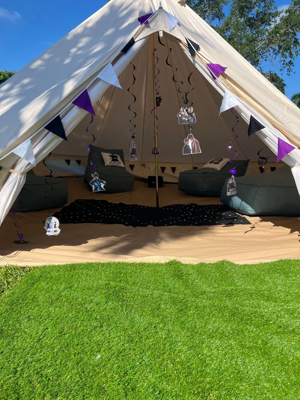 Large tent with open entrance, decorated with purple accents and paper lanterns inside, set on a lawn under clear skies for a Birthday celebration.