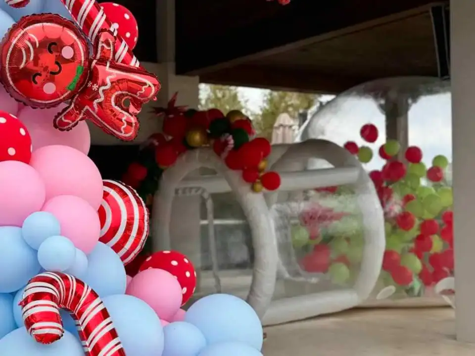 Colorful balloon arch with candy-themed decorations at a kids party entrance, partially obscuring a view of an inflated bounce house in the background.