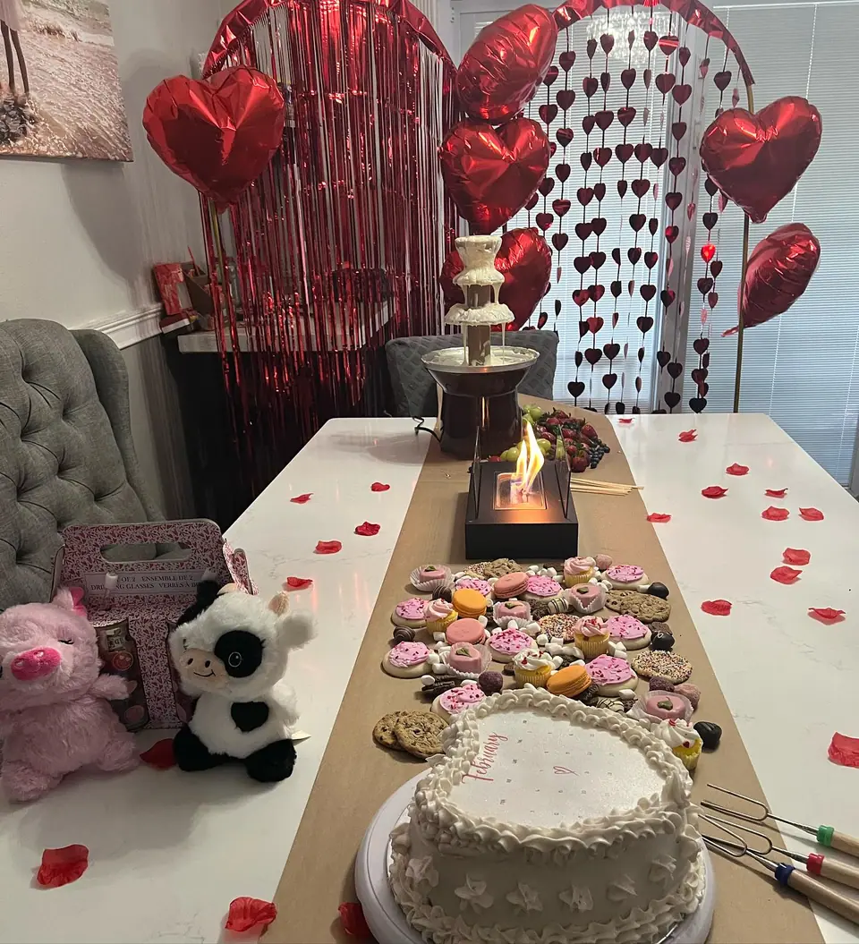A Valentine's Day themed table decorated with heart-shaped balloons, a red fringe curtain, assorted desserts, and a central flame, in a festive setting for the 2024 Ultimate Sleepover.