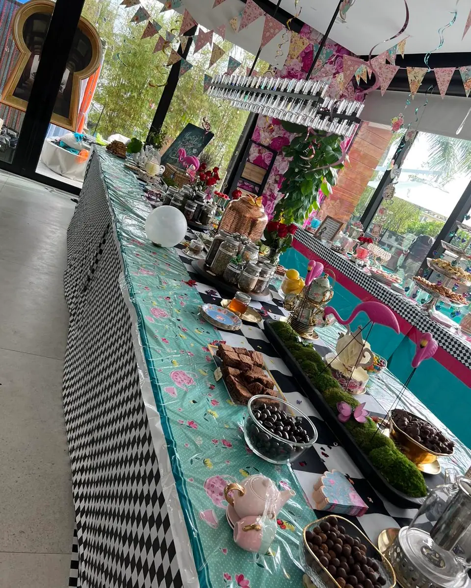 A long table set for an adult party extravaganza, adorned with colorful decorations, assorted foods, and a black and white checkered tablecloth.