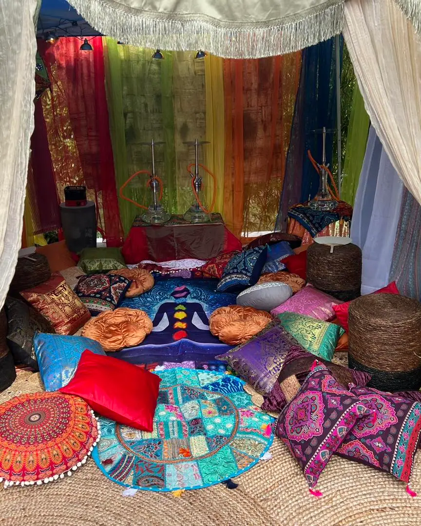 Colorful bohemian-style tent interior with assorted cushions, hanging drapes, and decorative rugs, creating a cozy, vibrant seating area for an ultimate night.