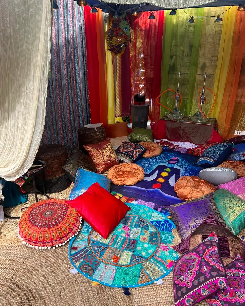 A colorful bohemian-style tent interior featuring an array of vibrant cushions, rugs, and draped fabrics, perfect for the ultimate adult party.