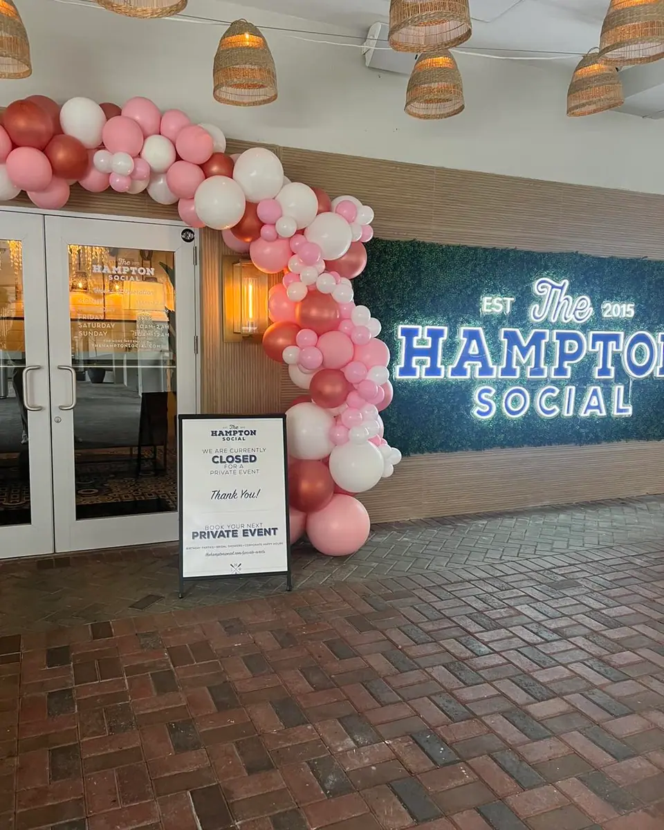 The Hampton Social entrance, adorned with a pink and white balloon arch from a local party shop, features a sign indicating the venue is closed for a private event.