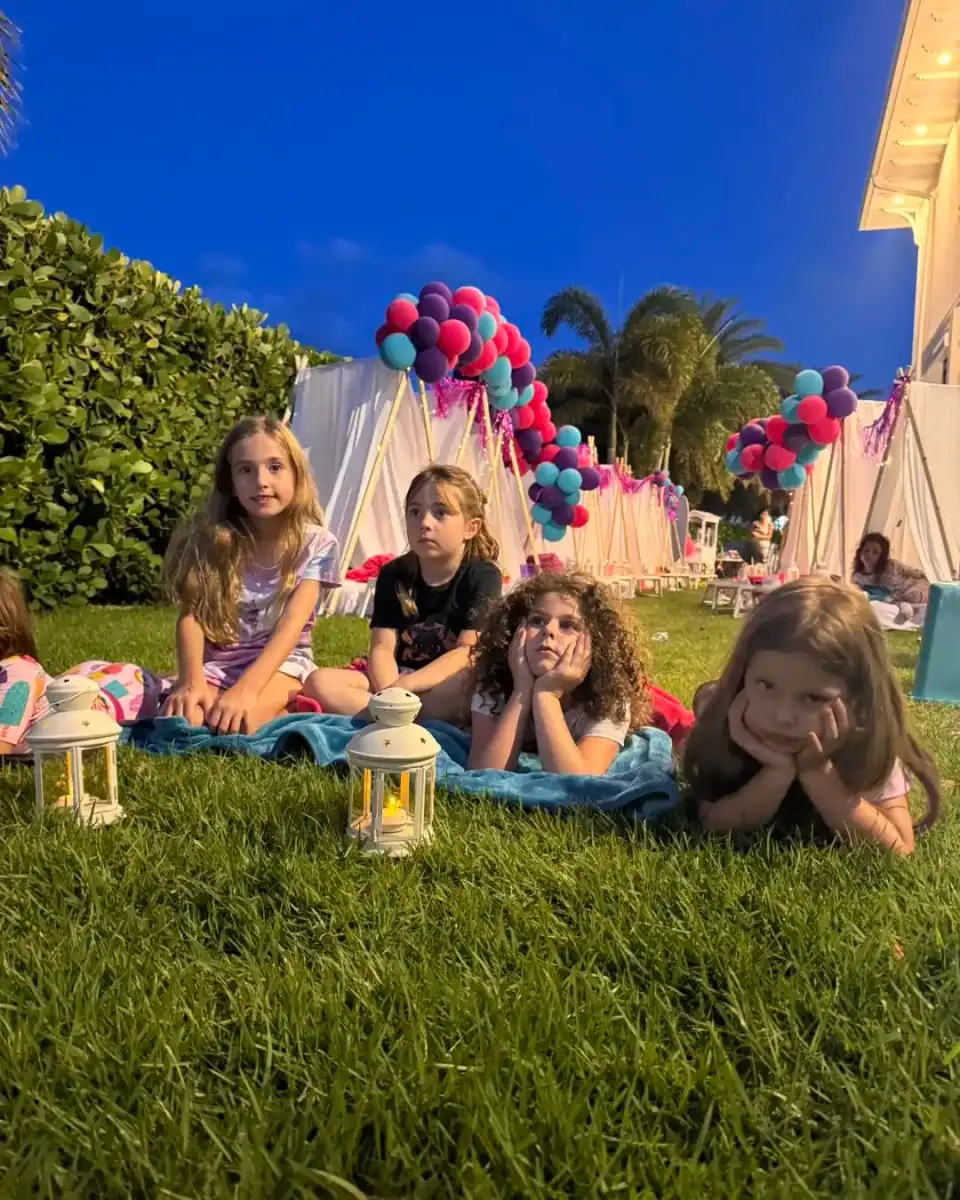 Four young girls relax on blankets at a Florida nighttime event with lanterns, tents, and balloons—an ideal scene for an unforgettable Outdoor Teepee Movie Party! kids party rental experience.