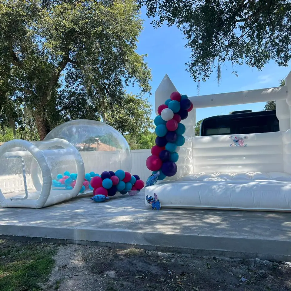 Discover the Ultimate Baby Shower Rentals setup featuring a captivating white inflatable bounce house paired with mesmerizing transparent spheres. This charming outdoor scene is adorned with an enchanting blend of blue, pink, purple, and white balloons that add a splash of color and fun. Set against a picturesque backdrop of lush green trees under a vibrant, sunny sky, this delightful arrangement promises to elevate any baby shower experience. Perfect for creating lasting memories and capturing Instagram-worthy moments, this curated rental ensemble is the ideal centerpiece for your celebration.