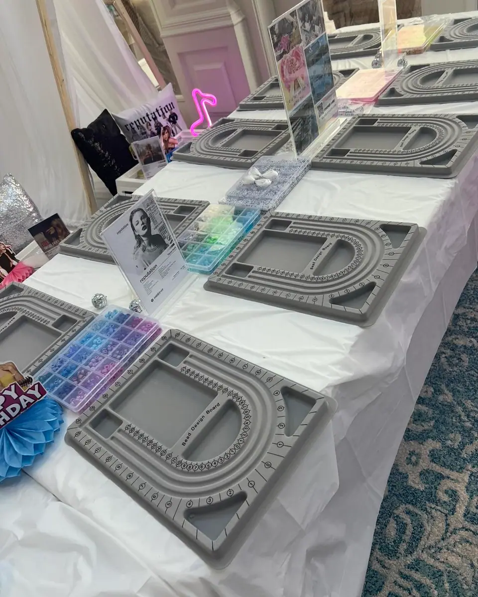 A table is set up with jewelry-making bead boards, containers of colored beads, tools, and instructions—perfect for a fun kids activity.