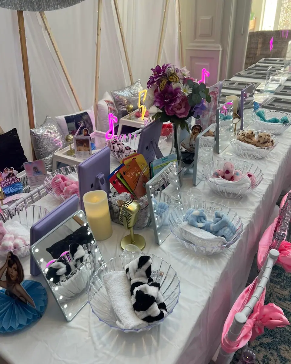 A long table set for a themed kids activity party, with mirrors, bowls of rolled towels, headbands, faux candles, flowers, and decorative items neatly arranged at each seat.