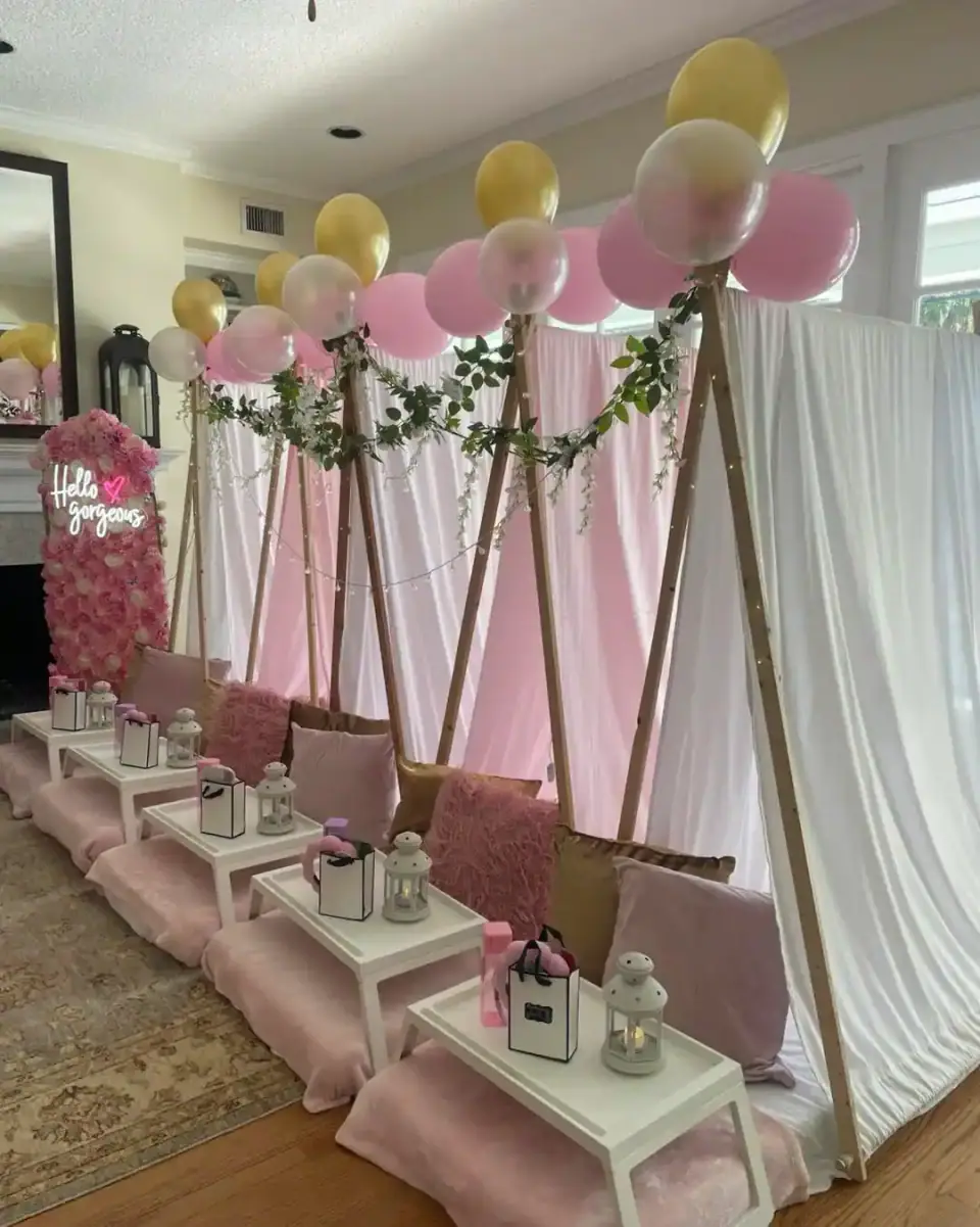 Indoor setup by a party shop in South Florida featuring small tents draped in white and pink fabric, decorated with pink and gold balloons, greenery, pillows, trays, and lanterns arranged on the floor.