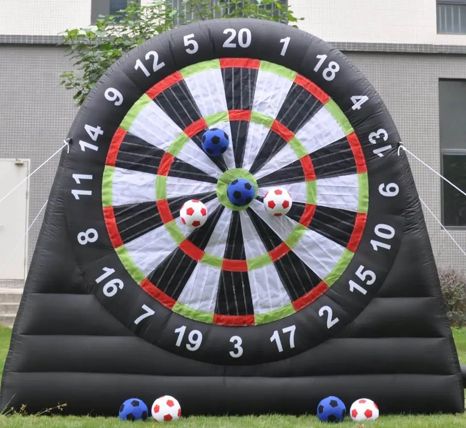 Inflatable dartboard with velcro soccer balls stuck on various numbers, located on a grass field in front of a building, perfect for birthday party add-ons.