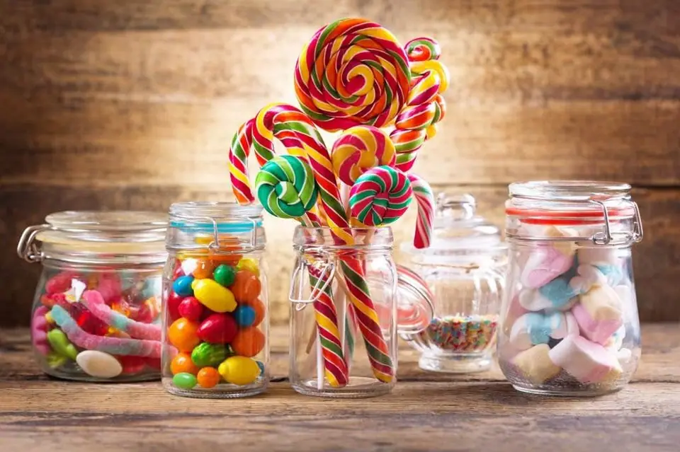 Assorted colorful candies and lollipops in clear jars on a wooden table for the ultimate slumber party.