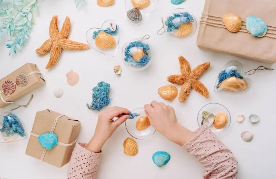 A person crafting with sea-themed materials, including starfish and shells, for a Mermaid Slumber Party, on a white surface.