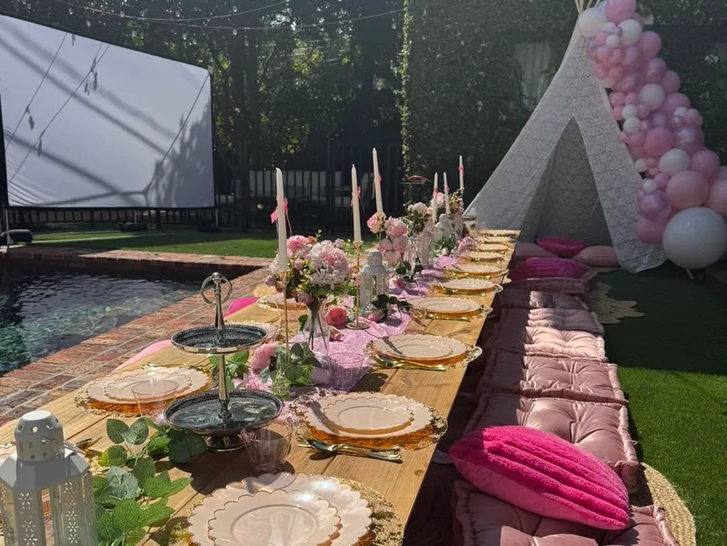 A Slumberr low picnic table with cushions, table settings and pink floral decorations in a garden.