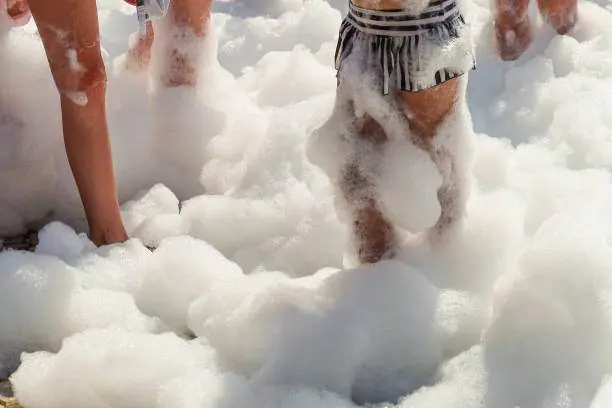 People stand in thick foam, with their legs partially covered by it, at a lively kids party rental.