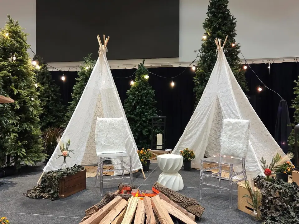 Two white teepees with a faux campfire and evergreen trees at a corporate event
