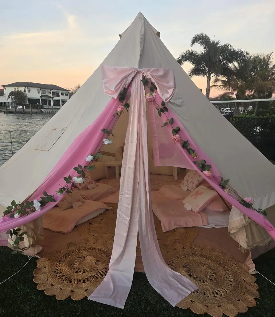 Slumberr bell tent with a pink bow and blush drapes on a waterfront lawn at sunset