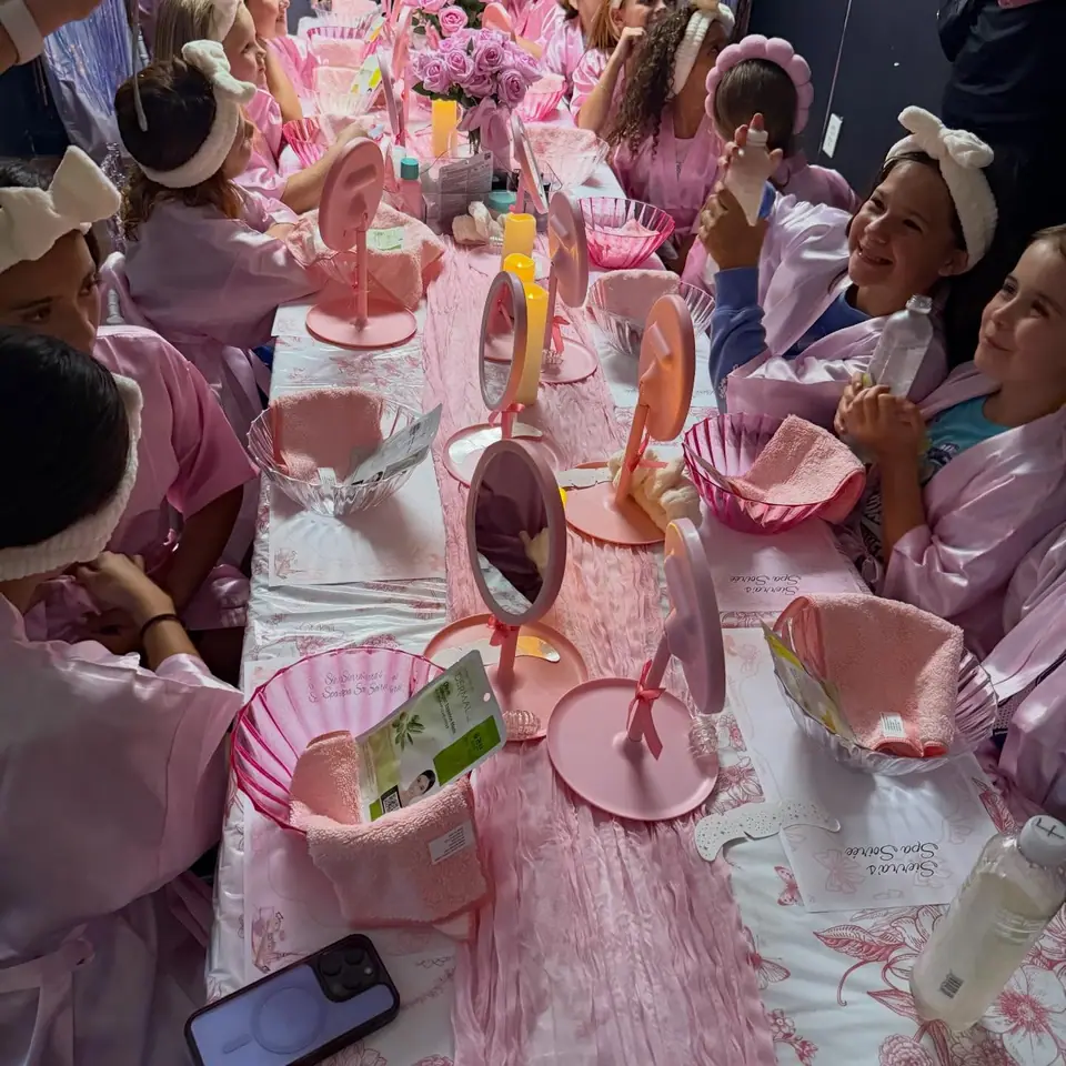 Girls in spa robes at a long pink table with mirrors
