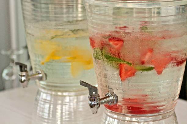 Two beverage dispensers filled with infused water sit side by side; one contains strawberries and mint, the other has lemon slices. Perfect for any slime party, each dispenser has a spout for easy serving.