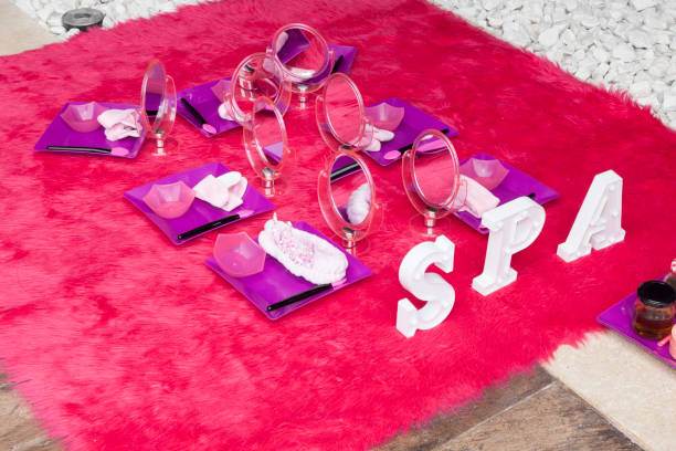 An arrangement of pink and purple spa supplies including mirrors, towels, and bowls, placed on a bright pink fuzzy surface with white "SPA" letters, perfect for a relaxing addition to your slime party service.