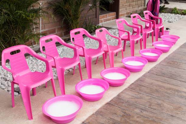A row of seven pink plastic chairs with matching pink basins filled with soapy water is set up outdoors on a paved area, perfectly prepared for a fun-filled slime party.