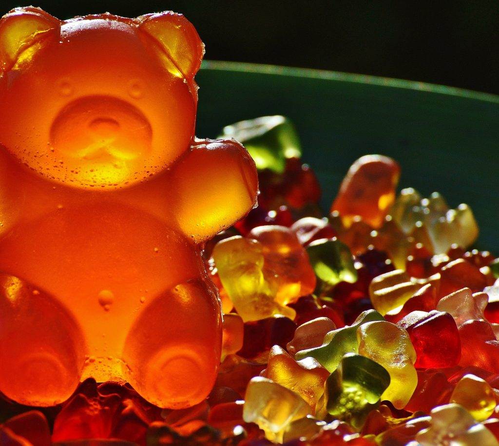 A large orange gummy bear stands on a surface covered with numerous smaller multicolored gummy bears, looking like the centerpiece for a fun kids party rental.
