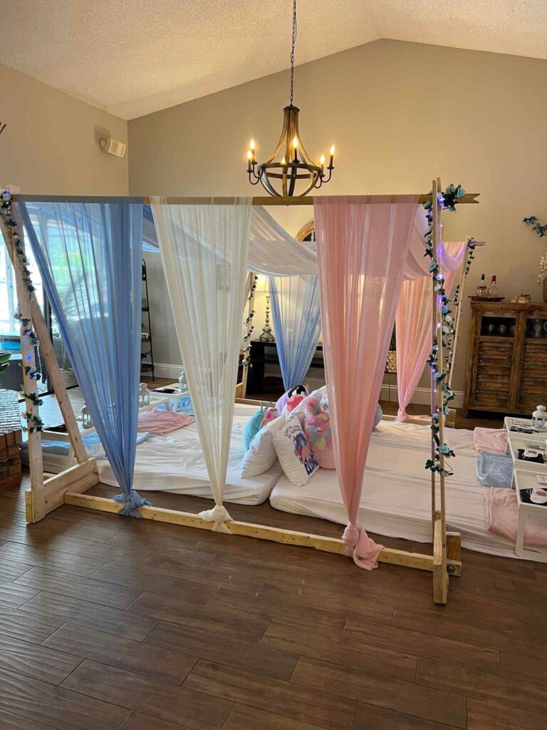 An ultimate canopy bed with white and pastel-colored sheer curtains in a room with decorative items and a chandelier.