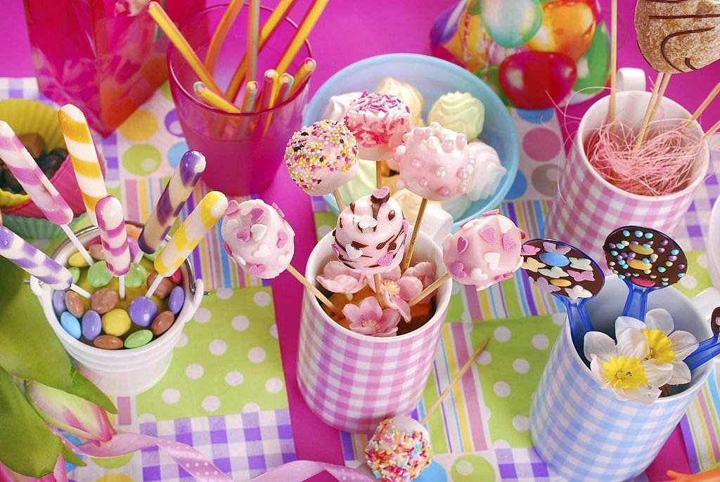 Assorted colorful candies and sweets displayed in decorative cups on a pastel plaid tablecloth at an ultimate canopy party.