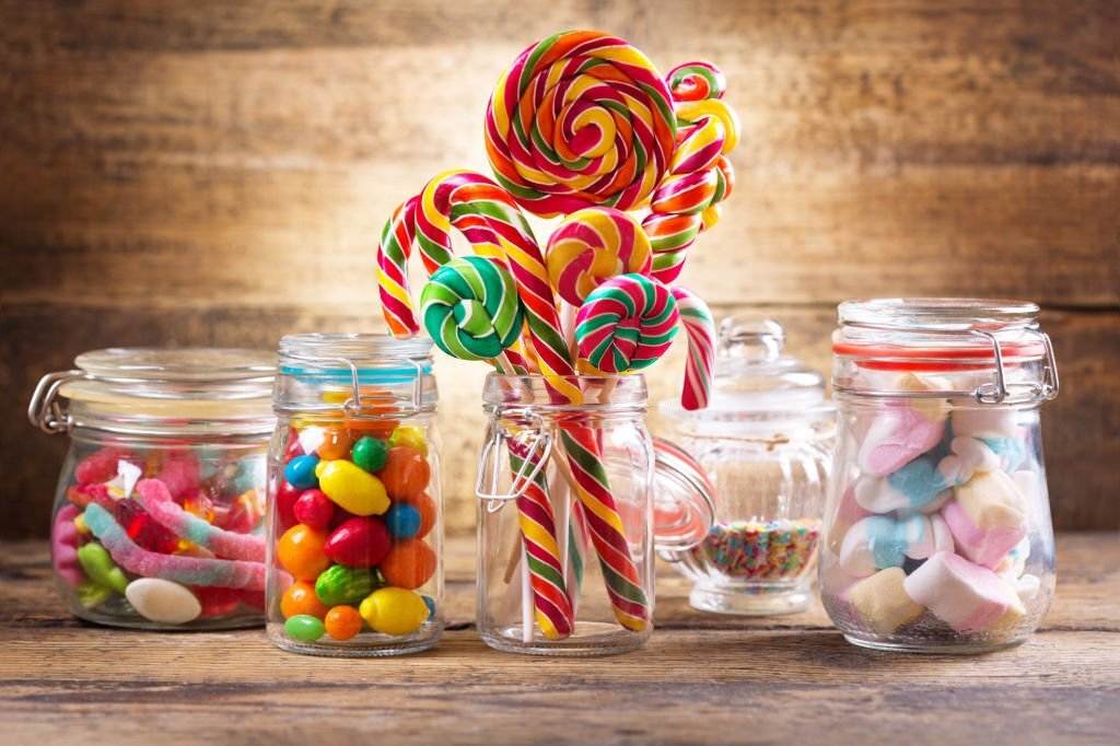 Assorted colorful candies and lollipops in clear jars on a wooden table for the ultimate slumber party.