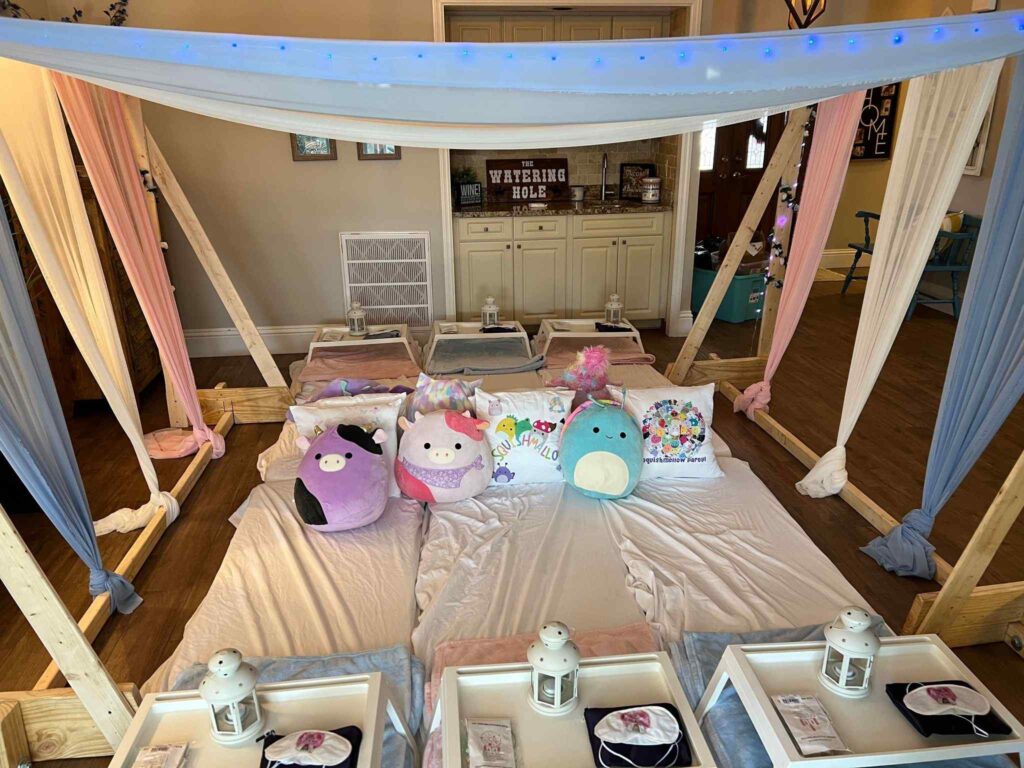 Indoor picnic setup with wooden tents, mattresses, and colorful pillows, fairy lights, and lanterns for a Slumber Party.
