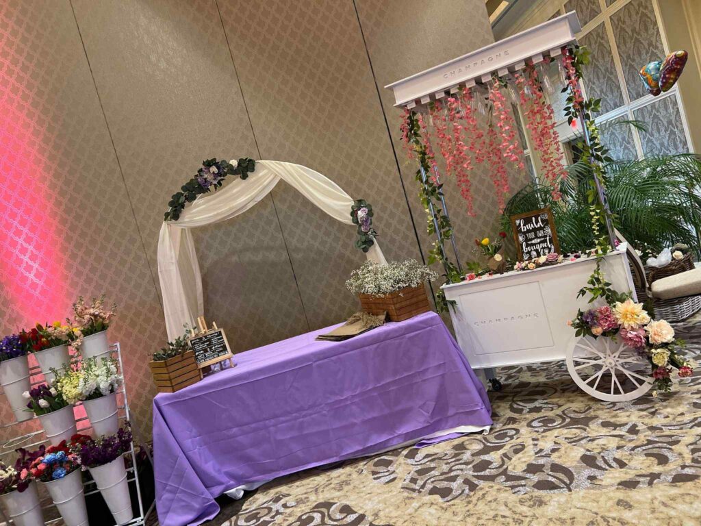 Wedding reception setup featuring a white cart, floral decorations, draped canopy, and a purple tablecloth in a decorated room for a Winter Haven party.