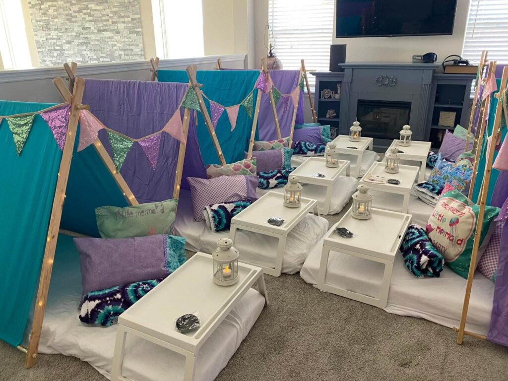 Indoor teepee-themed sleepover setup with small tents and lanterns in a living room.