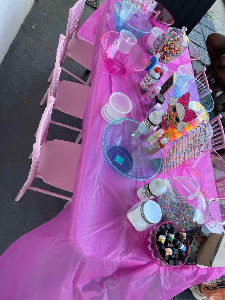 A table covered with a pink cloth, displaying various bottles of sprinkles and toppings for ice cream or desserts, perfect as a Birthday Party upgrade.