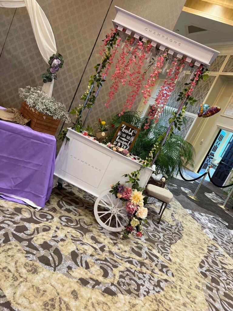 A decorative champagne cart adorned with flowers and a sign, stationed on a patterned carpet in a banquet hall, serving as an ultimate party upgrade.