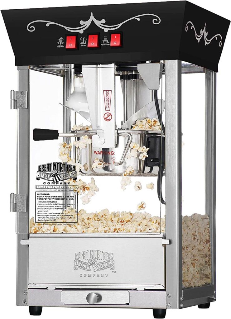 A commercial popcorn machine with a clear glass enclosure and stainless steel base, filled with freshly popped popcorn, perfect for birthday party add-ons.