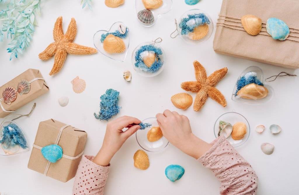 A person crafting with sea-themed materials, including starfish and shells, for a Mermaid Slumber Party, on a white surface.