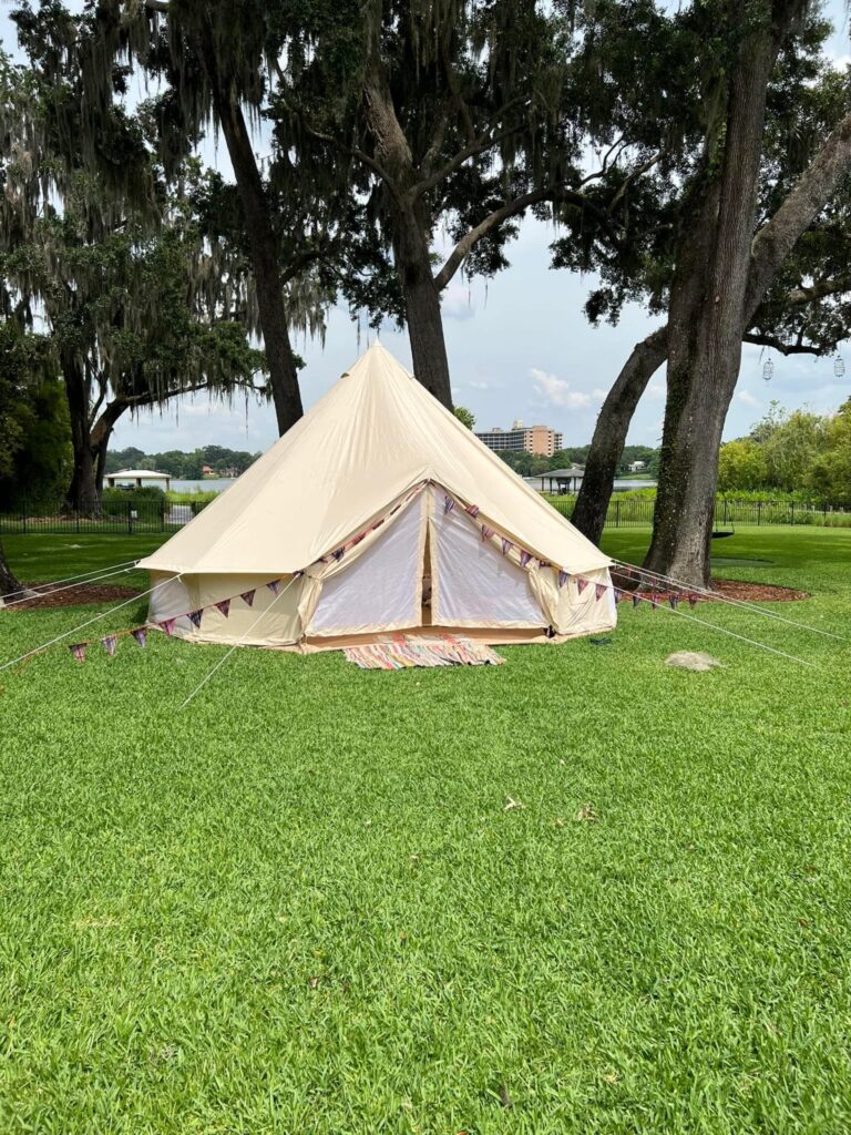 A canvas bell tent pitched on a grassy field with decorative bunting, surrounded by trees draped in Spanish moss and ready for a luxurious glamping experience.