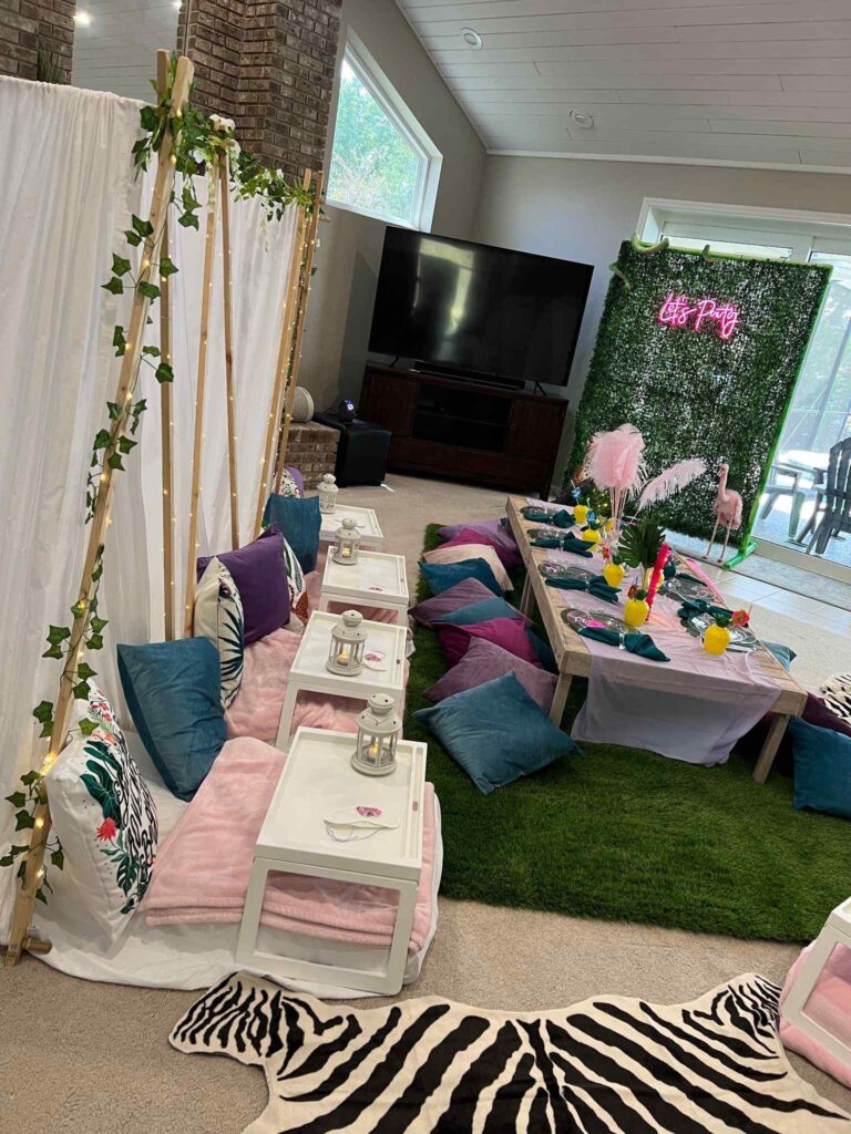 Indoor party setup with a tropical theme in Orlando, featuring a dining area with floor seating, colorful cushions, and a floral backdrop near a TV.