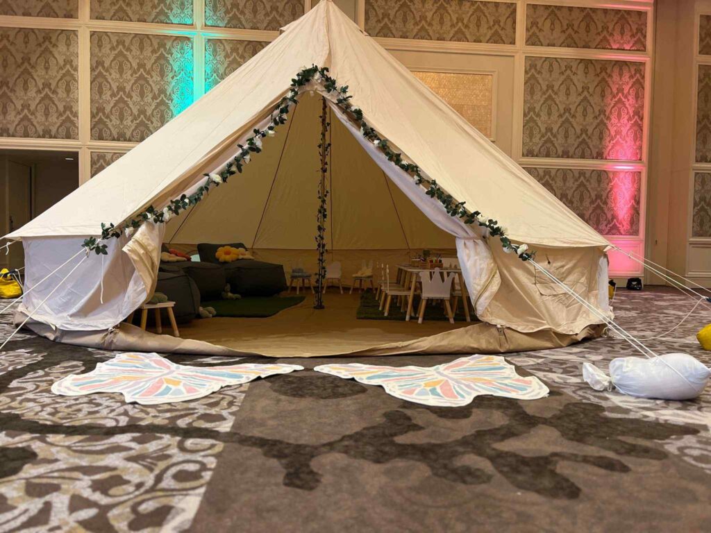 Large indoor tent designed for the ultimate sleepover, decorated with garlands and equipped with cozy furniture, set up in an elegant room with patterned carpet.