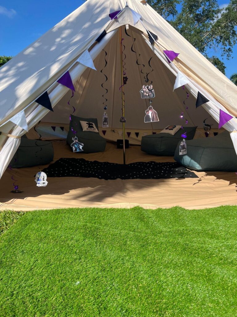 Large tent with open entrance, decorated with purple accents and paper lanterns inside, set on a lawn under clear skies for a Birthday celebration.