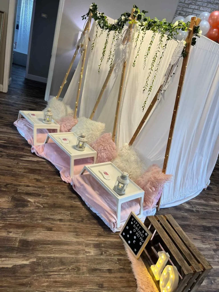 A decorative wedding swing setup with floral arrangements, wooden benches, and an enchanting teepee lantern, all set on a wooden floor inside a venue.