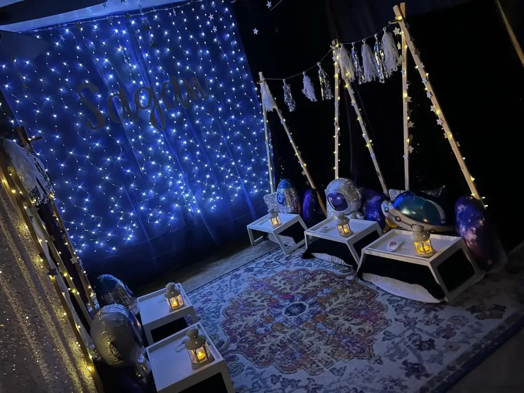 Dark-themed sensory room decorated with twinkling blue lights, hanging stars, and space-themed cushions on swings and an enchanting teepee.