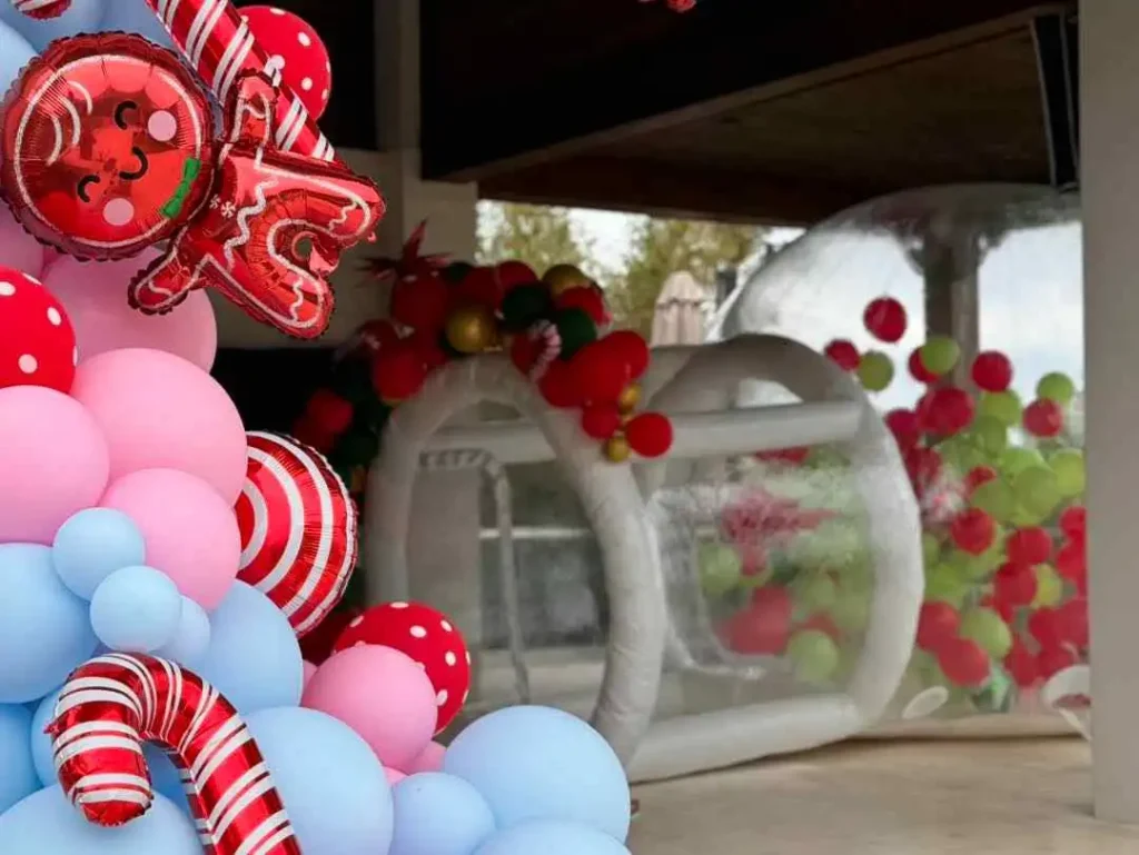 Colorful balloon arch with candy-themed decorations at a kids party entrance, partially obscuring a view of an inflated bounce house in the background.