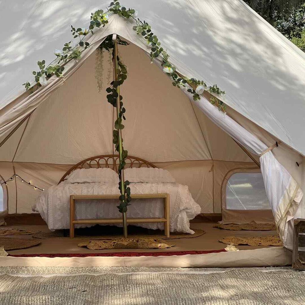 An elegantly decorated glamping tent with a white canopy, adorned with green vines and a plush bed inside, set in a natural environment, perfect for the ultimate slumber party.