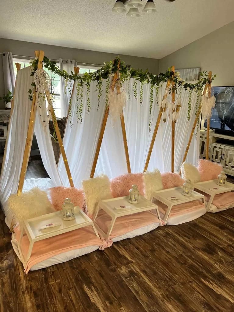 Indoor slumber setup with draped fabric tents over cushioned seats, adorned with greenery and hanging lanterns.