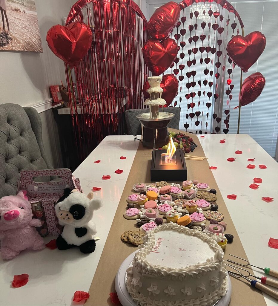 A Valentine's Day themed table decorated with heart-shaped balloons, a red fringe curtain, assorted desserts, and a central flame, in a festive setting for the 2024 Ultimate Sleepover.