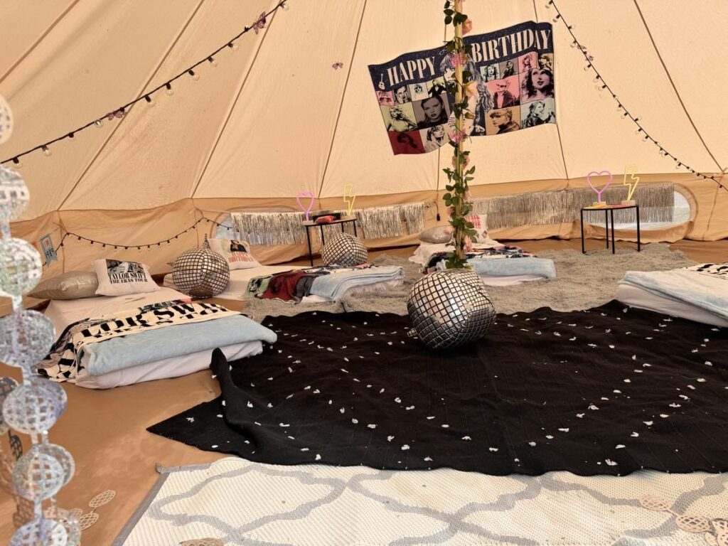 Interior of a tent with a birthday setup, featuring cushions, sleeping areas, and a "happy birthday" banner. Decor includes disco balls and a central decorative pole designed for the 2024 Ultimate Sleep